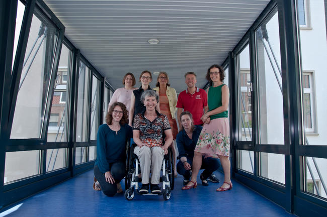 Auf dem Foto ist die Lenkungsgruppe des Netzwerk KulturInklusiv zu sehen. Es sind insgesamt 8 Personen mit und ohne Rollstuhl.