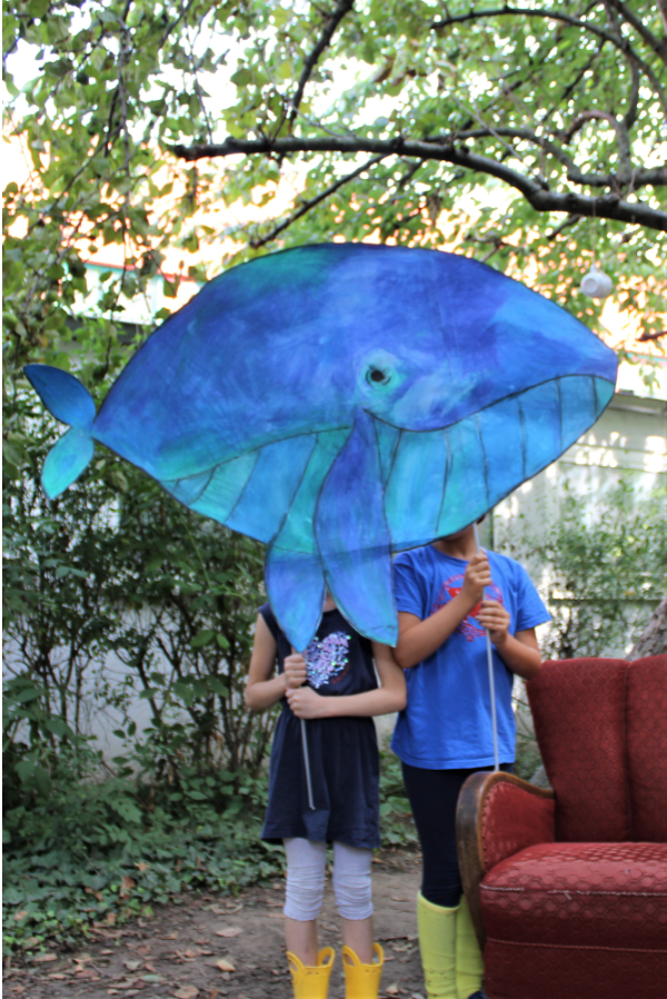 Zwei Kinder halten einen blauen Wal aus Pappe an zwei Stäben hoch
