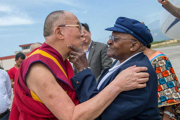 Zu sehen ist der Dalai Lama und der Erzbischog wie sie sich gegenüber stehen und freundschaftlich miteinander scherzen.